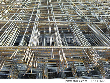 Folded metal construction mesh lies stacked atop each other, showcasing its intricate design. This sturdy material is often used for reinforcing concrete in various building projects. 133416680