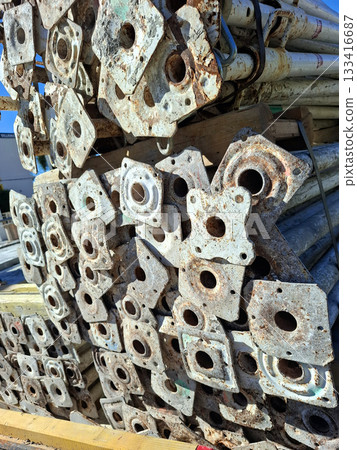 Metal construction supports are neatly stacked in an industrial yard. They show signs of wear and rust, indicating previous use. The scene captures the organized storage of construction materials. Metal construction supports are neatly stacked in an industrial yard. They show signs of wear and rust, indicating previous use. The scene captures the organized storage of construction materials. 133416687