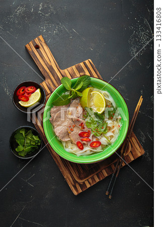 Vietnamese pho bo noodle soup beef lime asian bowl dinner black background wooden cutting board Vietnamese pho bo noodle soup beef lime asian bowl dinner black background wooden cutting board 133416808