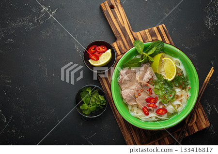 Vietnamese pho bo noodle soup beef lime asian bowl dinner black background wooden cutting board copy space 133416817