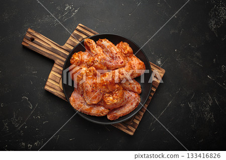 Raw marinated chicken wings spices garlic lemon black plate wooden cutting board cooking Raw marinated chicken wings spices garlic lemon black plate wooden cutting board cooking 133416826