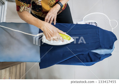 Senior citizens ironing student skirt and clothing in a house. Senior citizens ironing student skirt and clothing in a house. 133417455