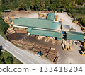 Aerial view of a sawmill factory in the mountains surrounded by dense forest, with stacks of processed lumber and timber 133418204