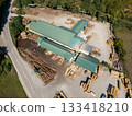 Aerial view of a sawmill factory in the mountains surrounded by dense forest, with stacks of processed lumber and timber 133418210