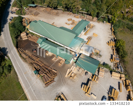 Aerial view of a sawmill factory in the mountains surrounded by dense forest, with stacks of processed lumber and timber 133418210