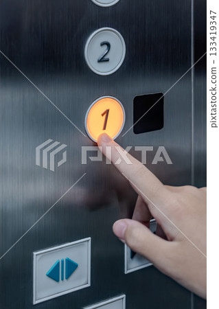The hand of a girl kid presses an elevator button, showing a finger pushing the button inside the elevator. The hand of a girl kid presses an elevator button, showing a finger pushing the button inside the elevator. 133419347