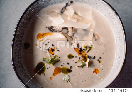 A delightful creamy mushroom soup served in a bowl, topped with cheese and herbs. A soup garnished with parmesan cheese and microgreens, ready to eat. 133419374