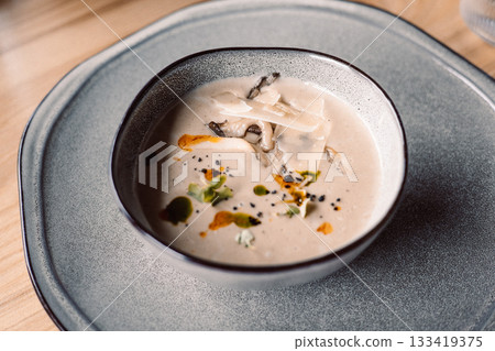 A delightful creamy mushroom soup served in a bowl, topped with cheese and herbs. A soup garnished with parmesan cheese and microgreens, ready to eat. 133419375