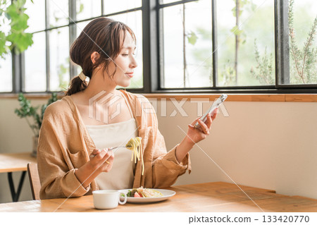 Young Asian woman looking at her smartphone while having lunch in a cafe 133420770