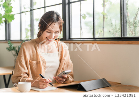 Young Asian woman taking notes using tablet and smartphone in cafe 133421081