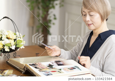 一位老婦人將孫輩和子女的照片放入相冊 133421564