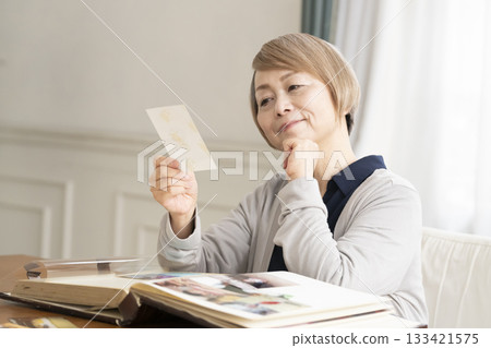 一位老婦人將孫輩和子女的照片放入相冊 133421575