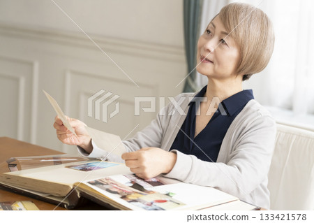 Senior woman putting photos of her grandchildren and children into an album Senior woman putting photos of her grandchildren and children into an album 133421578