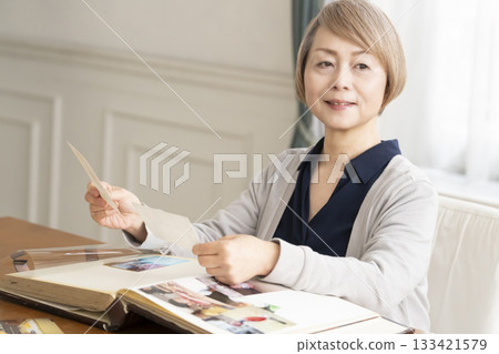 Senior woman putting photos of her grandchildren and children into an album Senior woman putting photos of her grandchildren and children into an album 133421579