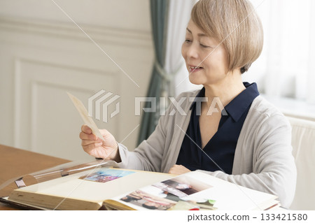 一位老婦人將孫輩和子女的照片放入相冊 133421580