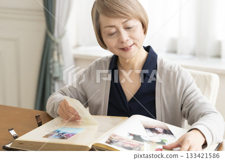 一位老婦人將孫輩和子女的照片放入相冊 133421586