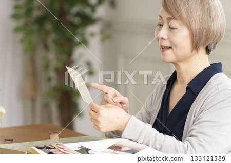 一位老婦人將孫輩和子女的照片放入相冊 一位老婦人將孫輩和子女的照片放入相冊 133421589