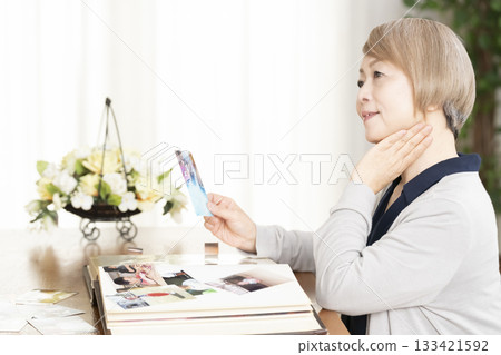 一位老婦人將孫輩和子女的照片放入相冊 133421592