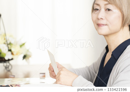 一位老婦人將孫輩和子女的照片放入相冊 133421596