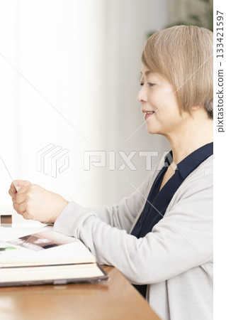 Senior woman putting photos of her grandchildren and children into an album 133421597