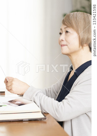 一位老婦人將孫輩和子女的照片放入相冊 133421598