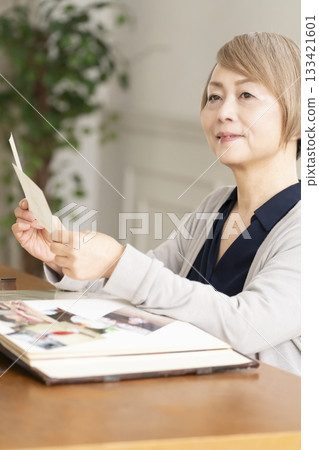 一位老婦人將孫輩和子女的照片放入相冊 133421601