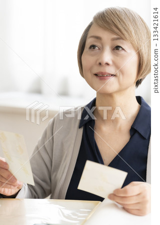 一位老婦人將孫輩和子女的照片放入相冊 133421614