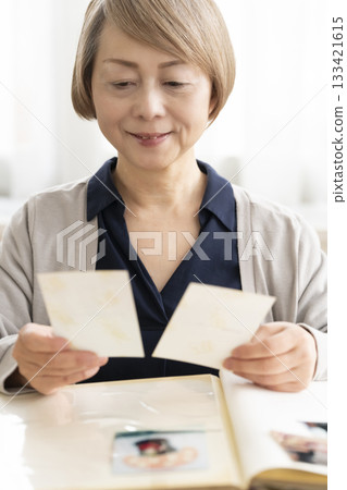 一位老婦人將孫輩和子女的照片放入相冊 133421615