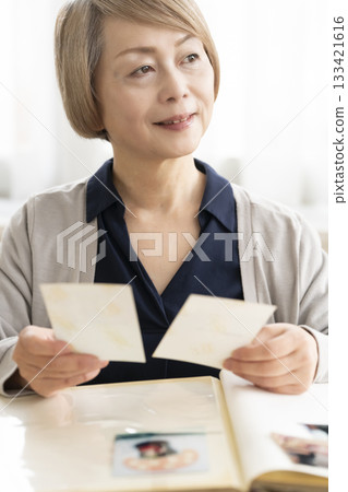 一位老婦人將孫輩和子女的照片放入相冊 133421616