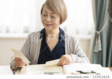 一位老婦人將孫輩和子女的照片放入相冊 一位老婦人將孫輩和子女的照片放入相冊 133421618