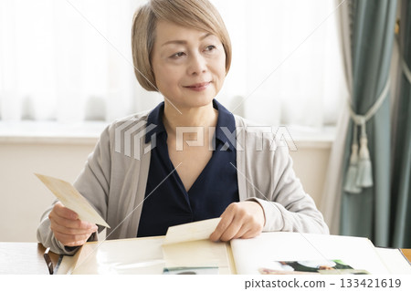 Senior woman putting photos of her grandchildren and children into an album 133421619
