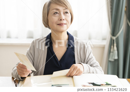 一位老婦人將孫輩和子女的照片放入相冊 133421620