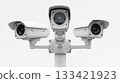 Three white security cameras mounted on a pole are observing the surroundings. This modern electronic surveillance system provides constant public safety and digital protection outdoors. 133421923