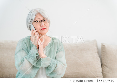 A gray-haired senior woman with a troubled expression while talking on her smartphone (scam call, suspicious call, nuisance call) A gray-haired senior woman with a troubled expression while talking on her smartphone (scam call, suspicious call, nuisance call) 133422659