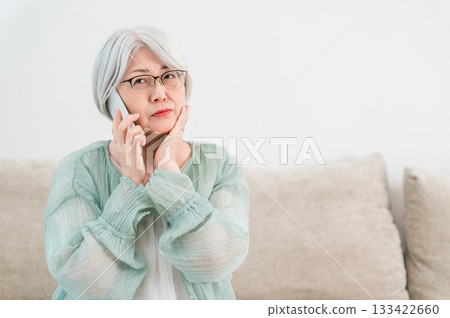 一位頭髮花白的老婦人，神情憂慮地用智慧型手機通話（詐騙電話、可疑電話、騷擾電話） 133422660