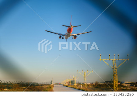 The image shows a commercial airplane on its final approach for landing, with the landing gear down. It's flying low over a runway approach path, with approach lighting clearly visible on each side 133423280