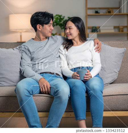 一對日本夫婦在客廳沙發上放鬆地擁抱在一起。 一對日本夫婦在客廳沙發上放鬆地擁抱在一起。 133423512