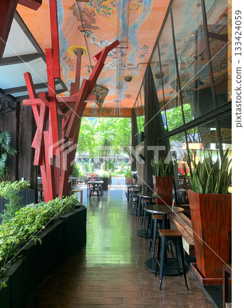 Modern cafe interior with wooden beams, tables, and lush greenery Modern cafe interior with wooden beams, tables, and lush greenery 133424059