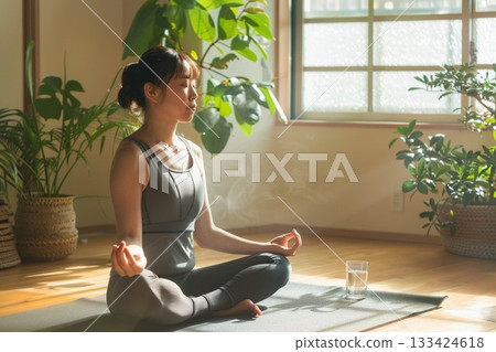 A healthy young woman doing yoga and stretching in the living room in the morning to improve her mind and body A healthy young woman doing yoga and stretching in the living room in the morning to improve her mind and body 133424618