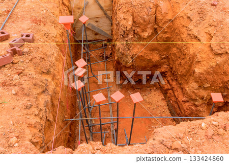 Workers are digging trench setting up steel rebar for new building foundation in suburb. 133424860