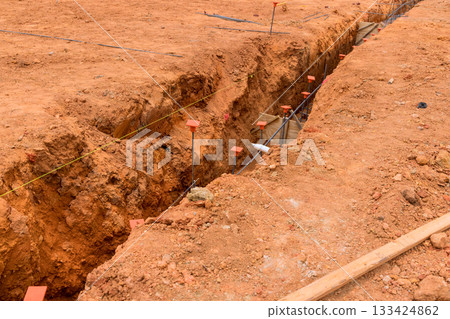 Workers prepare for building by digging trench in dry terrain, marked for accurate foundation placement. Workers prepare for building by digging trench in dry terrain, marked for accurate foundation placement. 133424862