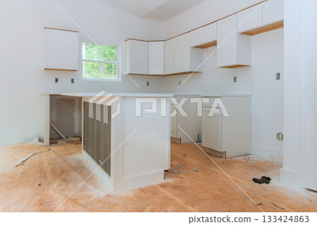 Renovation work is underway in kitchen featuring new white cabinets wooden flooring waiting for completion. 133424863