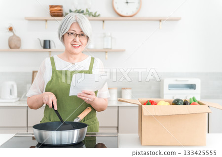 Senior woman (smiling) cooking with meal kit or cooking kit in her kitchen at home 133425555