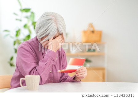 A worried, gray-haired senior woman is troubled by her savings passbook (financial troubles, bankruptcy in old age, personal bankruptcy) 133426315