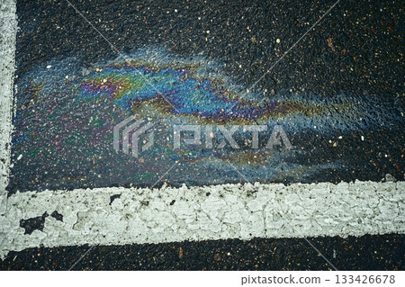 Oil slick spreads rainbow colors on wet dark asphalt next to a white line Oil slick spreads rainbow colors on wet dark asphalt next to a white line 133426678