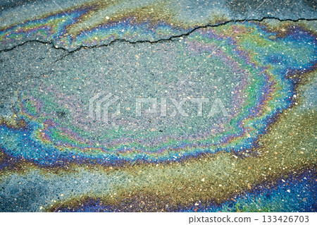 Oil puddle displaying a vibrant iridescent color spectrum on cracked asphalt Oil puddle displaying a vibrant iridescent color spectrum on cracked asphalt 133426703