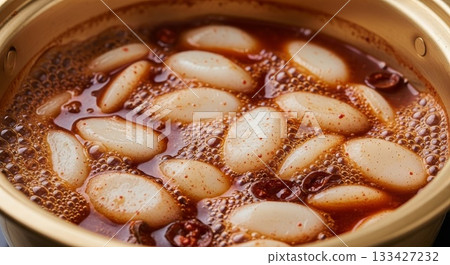 Traditional Korean rice cakes floating in bubbling spicy gochujang broth inside ceramic earthenware pot with red pepper flakes 133427232