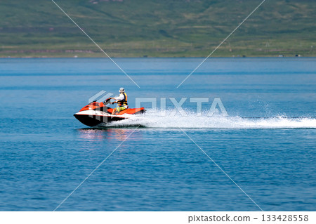A man in a life jacket floats on a scooter on a lake. 133428558