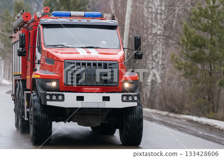 A red fire truck drives along a country road in winter. 133428606