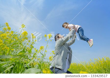 一位父親抱著女兒走在兩旁開滿油菜花的林蔭大道上。 133429517